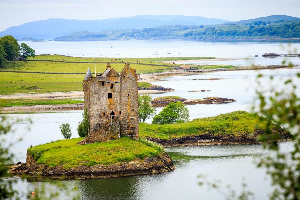 The beautiful shot of Castle Stalker from afar with greenery and water all around.